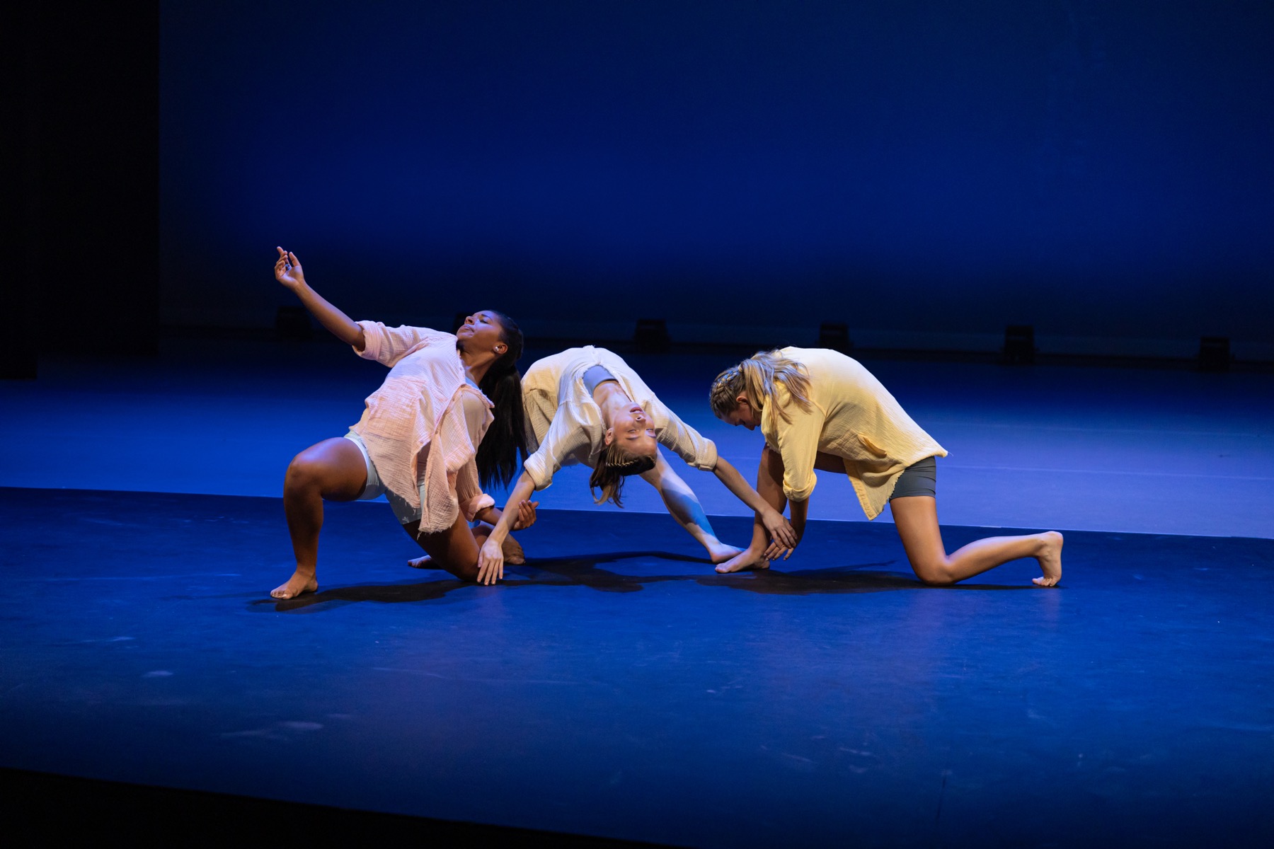 Falling Down trio performing a low floorwork phrase on a blue-lit stage