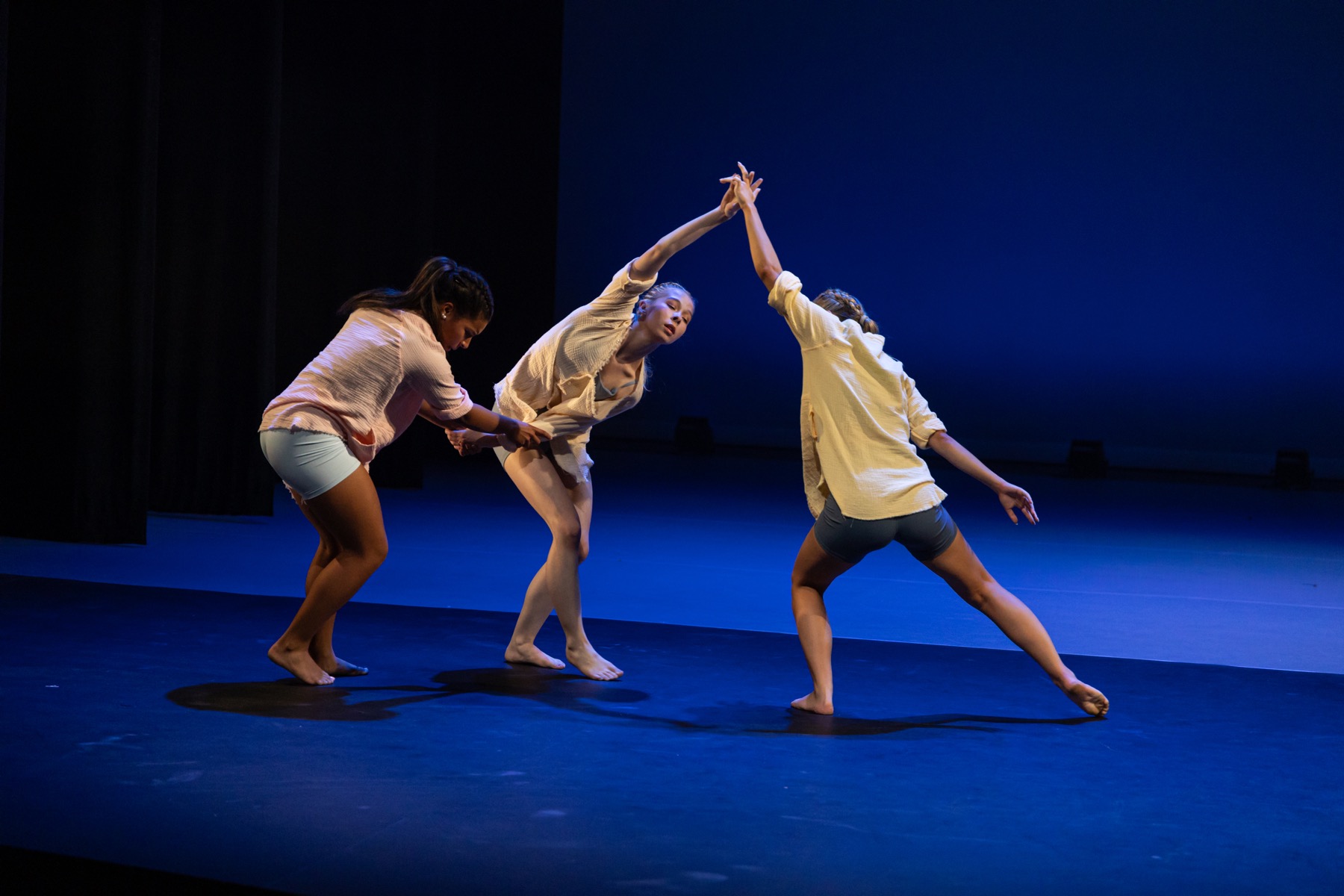 Falling Down trio holding hands in a diagonal phrase under blue lighting