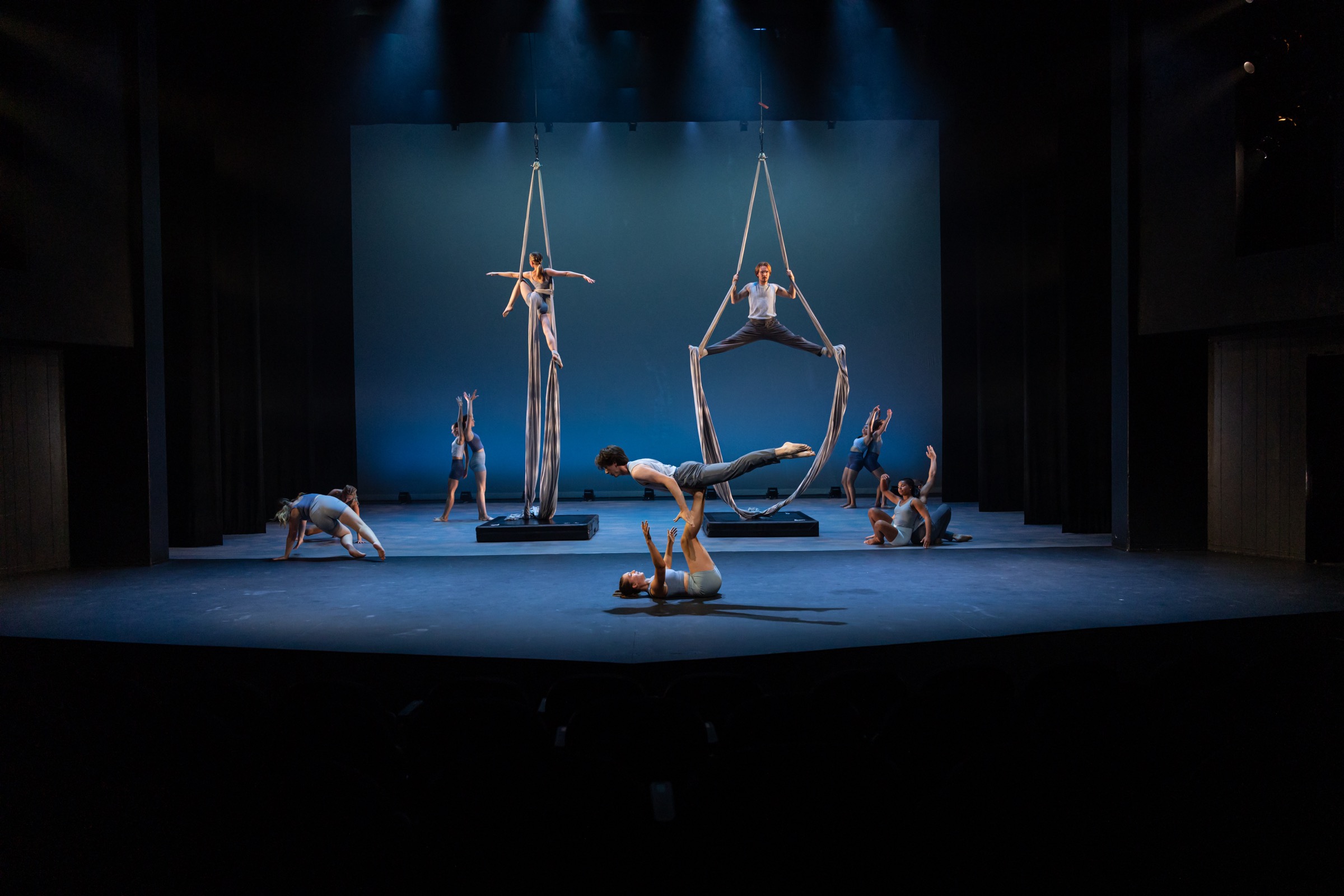 Flying/Falling ensemble performing aerial and floorwork across a blue stage