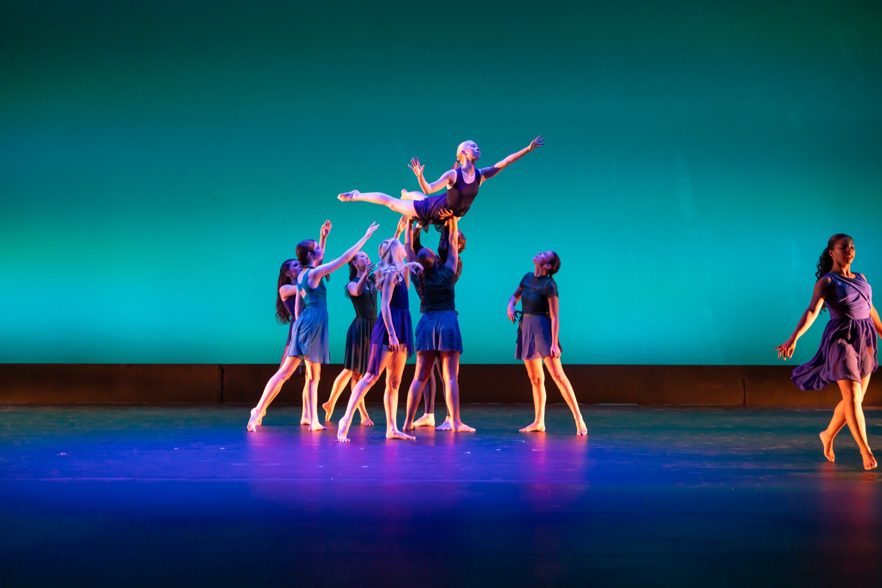 A Lamp to My Feet ensemble lifting a dancer under teal stage lighting