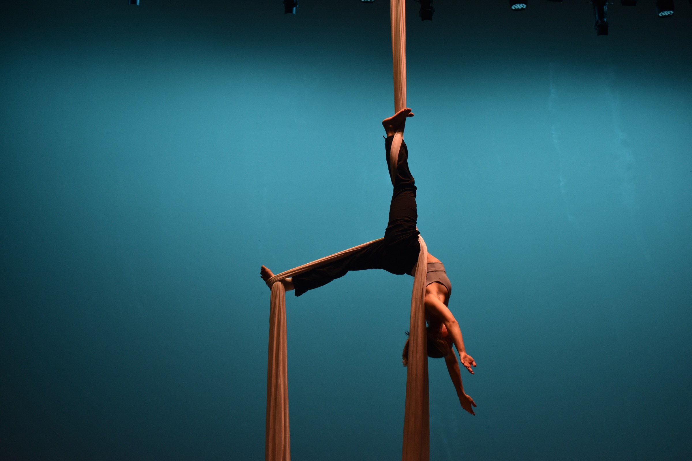Aerial fabric rehearsal with a dancer inverted against a teal stage backdrop