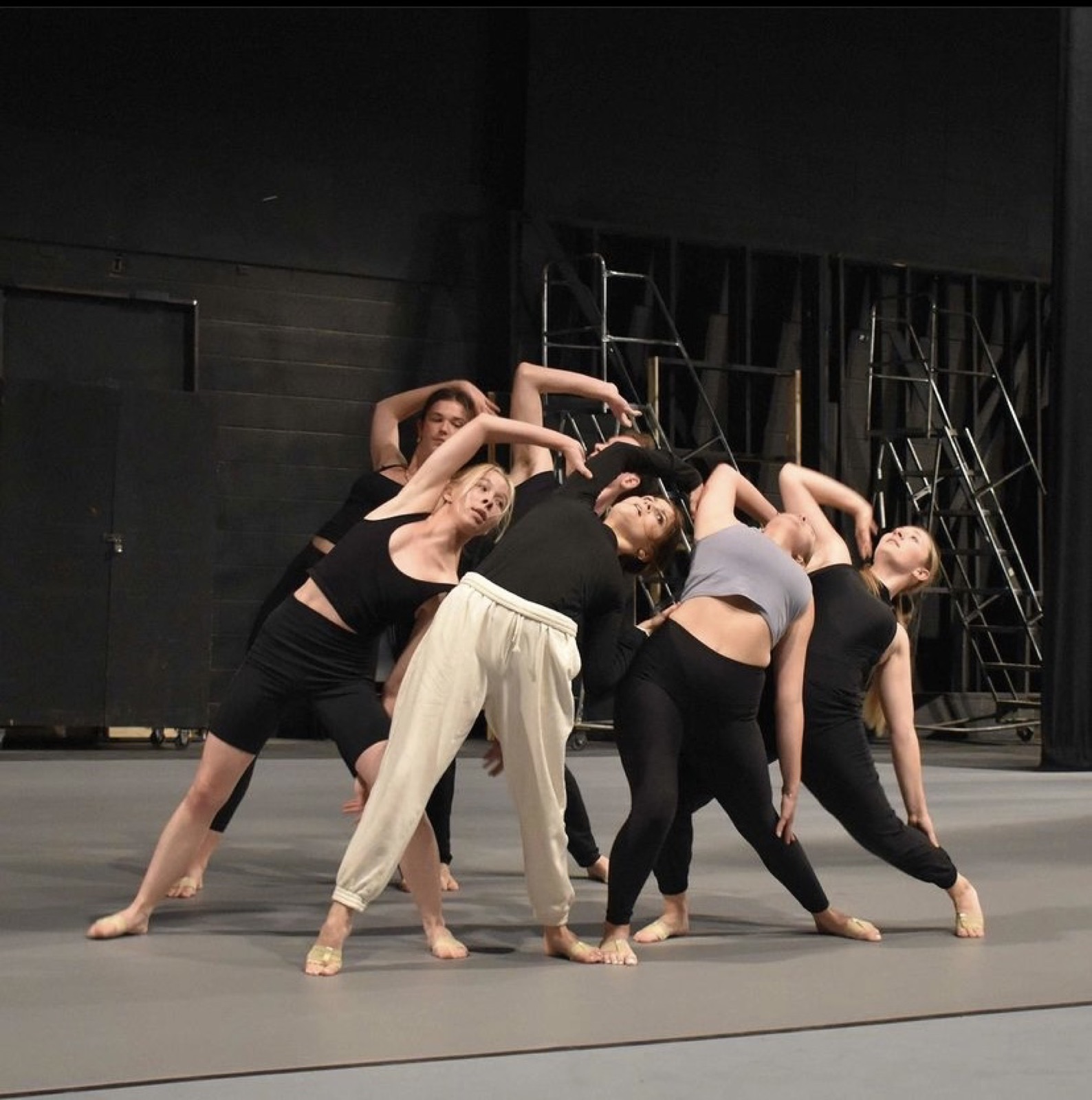 Dance rehearsal group leaning into a connected shape in black practice clothes