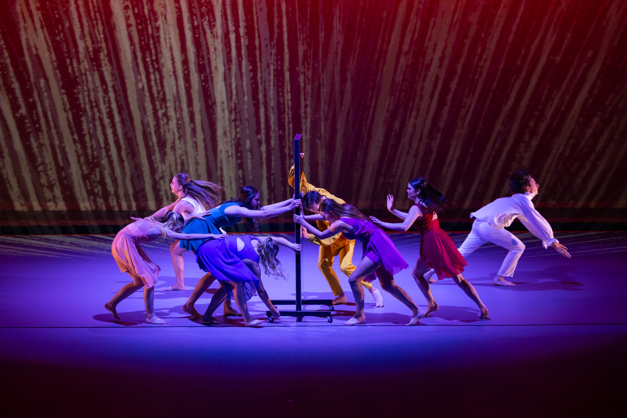 Strife ensemble pushing a mirror prop across a purple-lit stage