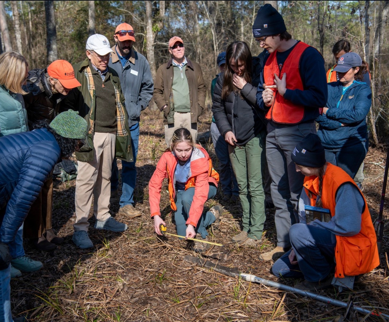 Liz Koifman in an orange jacket measuring vegetation during fieldwork